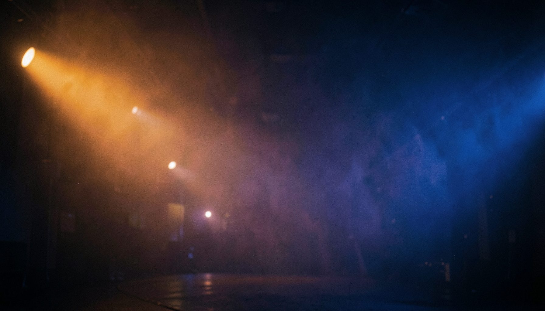 Warm amber and deep indigo stage lights glowing through atmospheric haze, wide cinematic frame