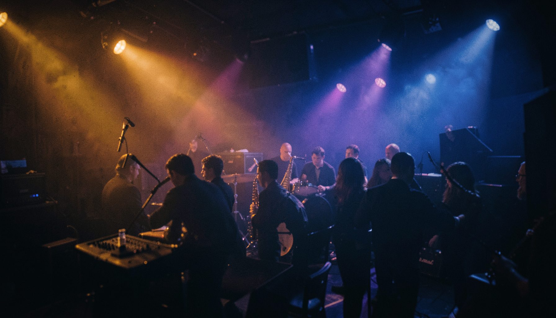 Warm amber and deep indigo stage lights glowing through atmospheric haze over a jazz club interior