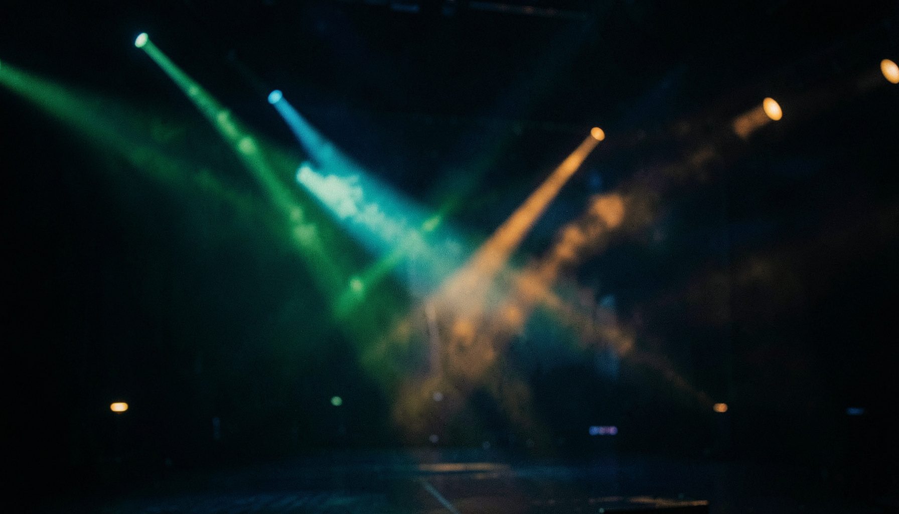 Deep emerald and warm amber intersecting light beams across a dark stage