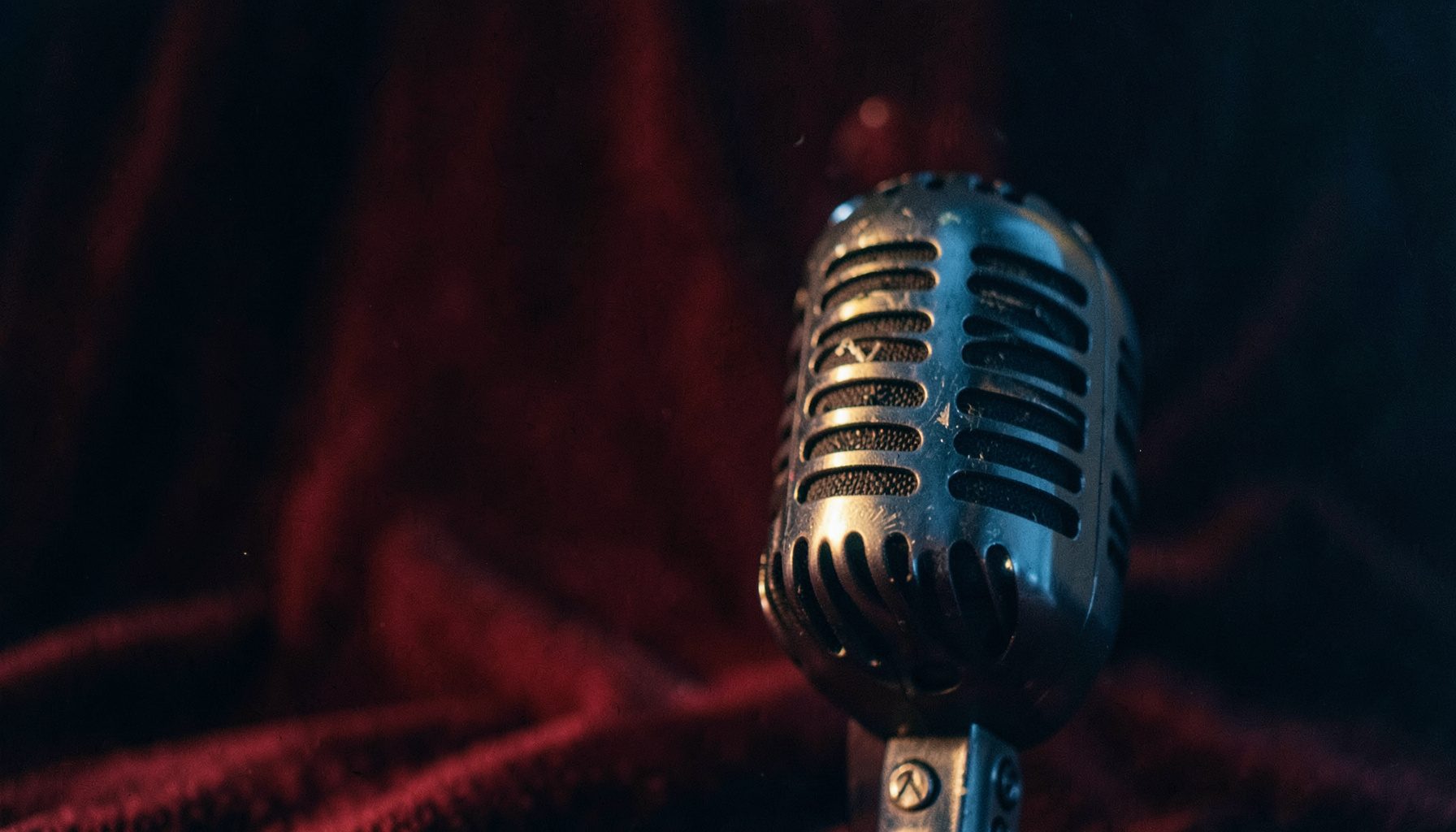 Vintage microphone against a deep burgundy backdrop, warm tungsten glow