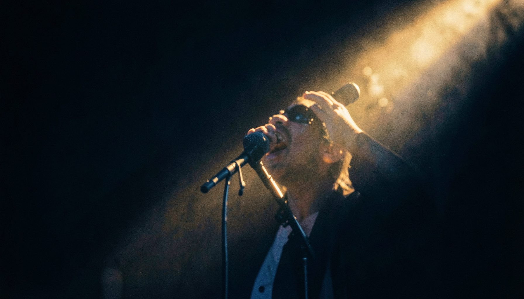Jazz vocalist microphone on stage caught in a shaft of warm golden light against a dark background